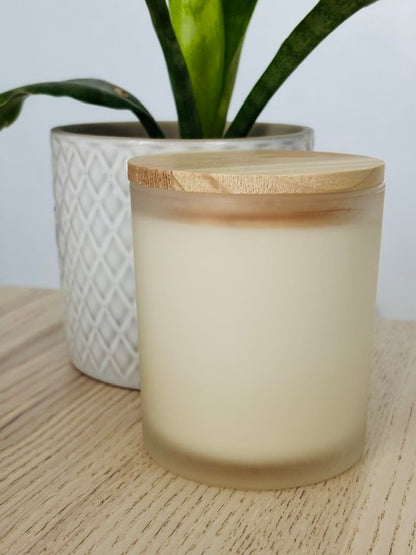 Frosted glass candle with wooden lid on a wooden surface, with a plant in the background.